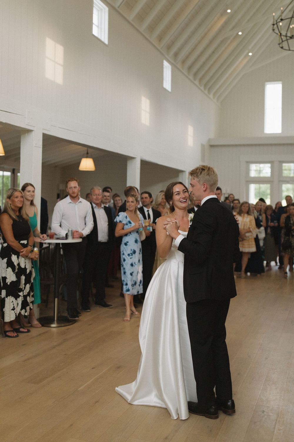 Wedding couples dance in a spacious white chapel with wooden floors and vaulted ceilings.