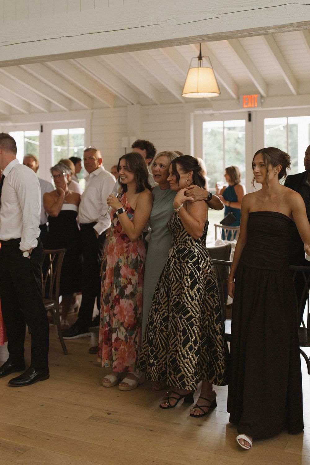 Wedding guests gather and socialize in an elegant white chapel with wooden floors.
