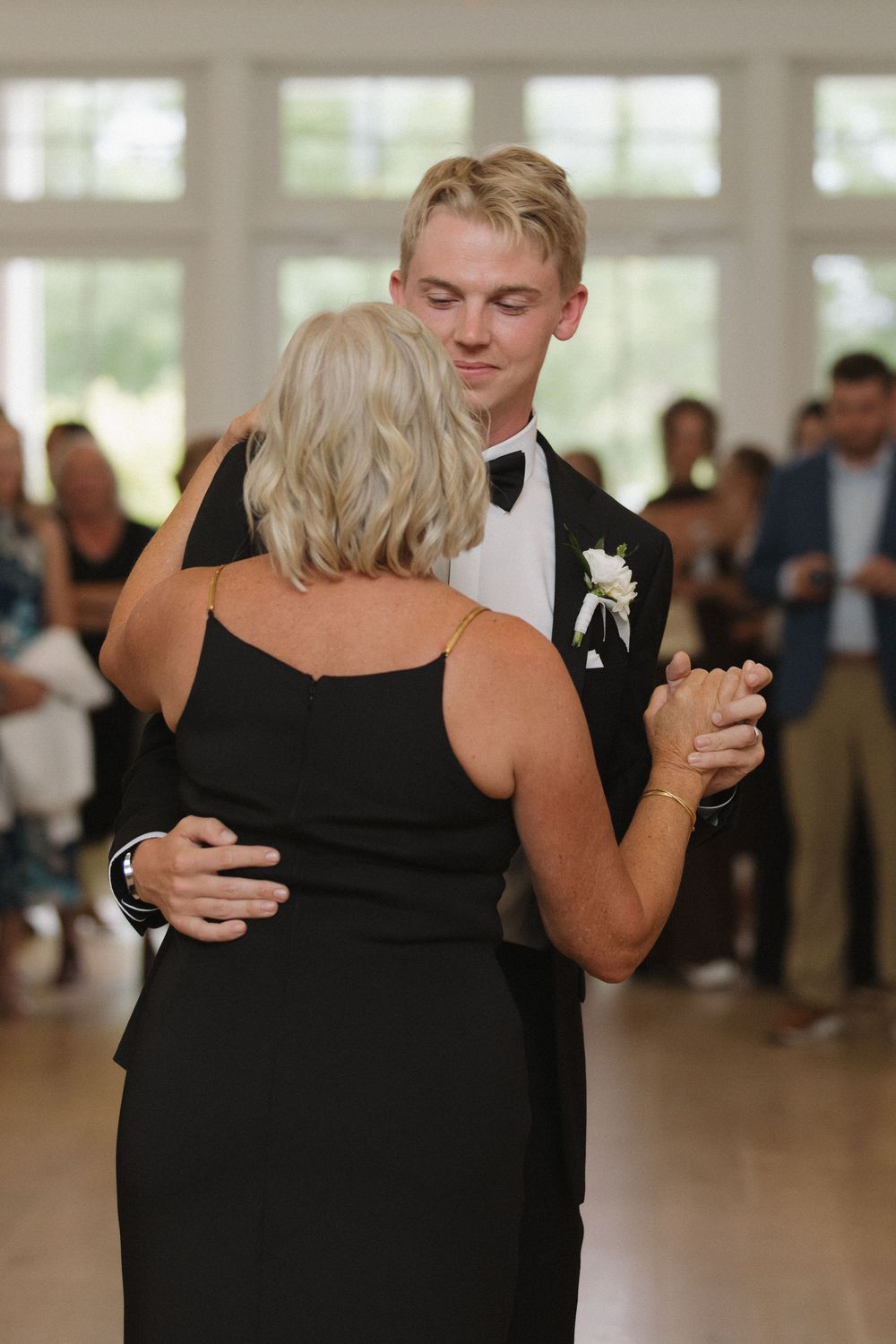 Wedding guests in formal attire dancing together in a bright reception venue.