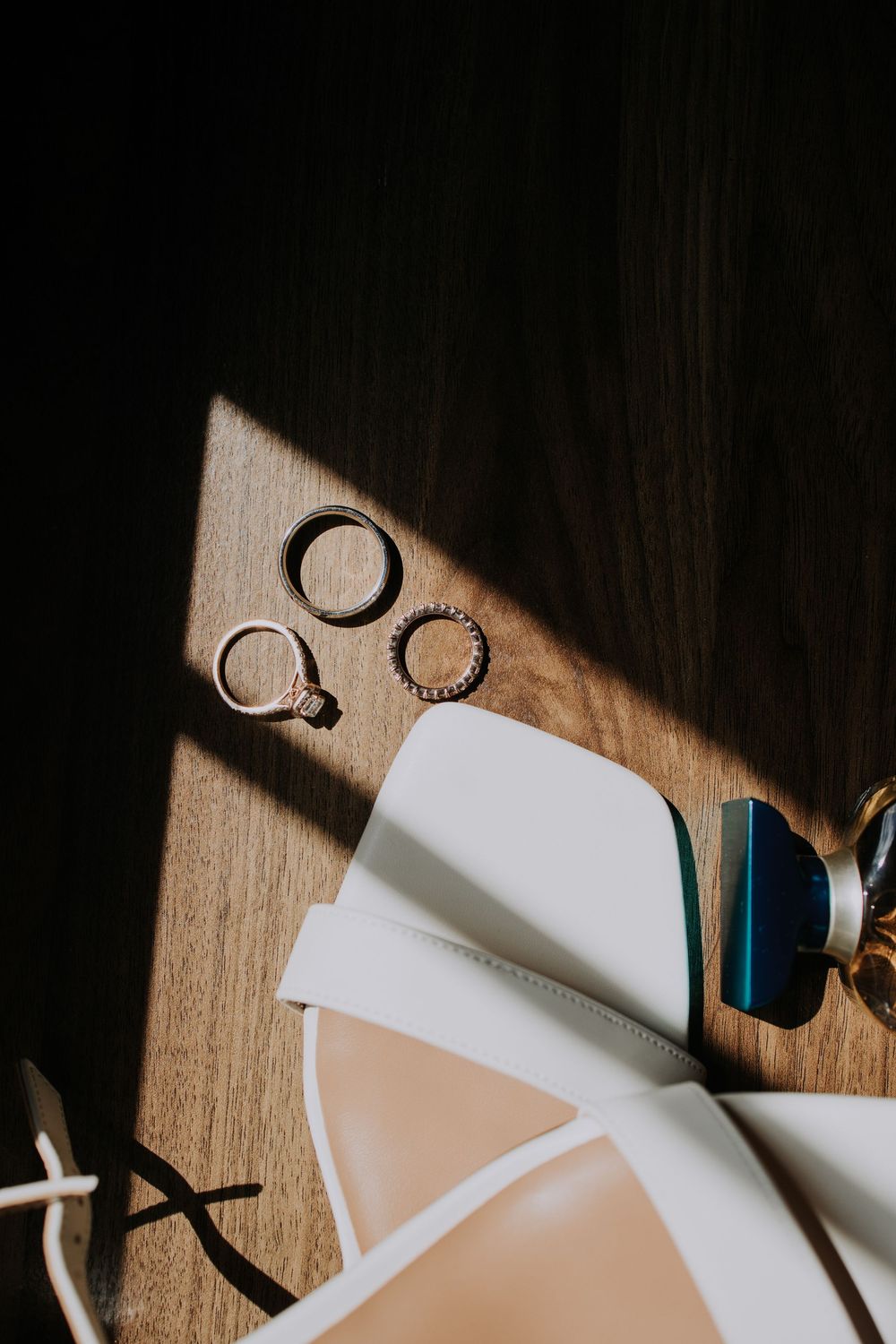 Diagonal shadows cast across white paper and wooden surface with scattered office supplies and rings in moody lighting.