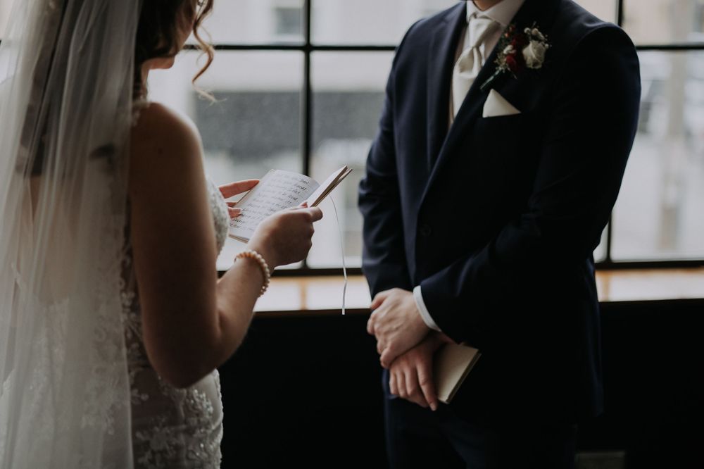 Bride reading wedding vows to groom in navy suit during intimate indoor ceremony.