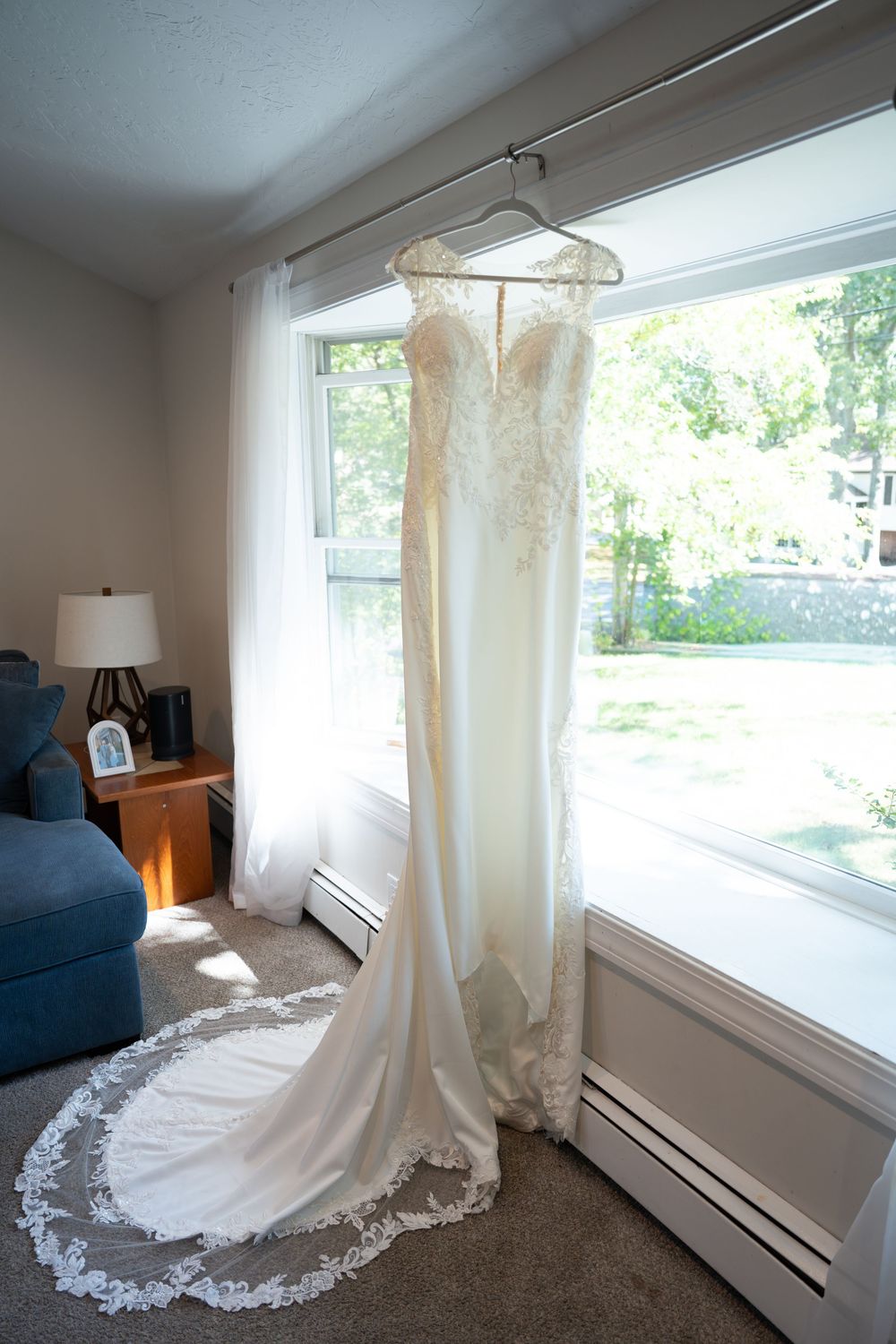 A beautiful white wedding dress with intricate lace details and long train displayed in a sunlit room.