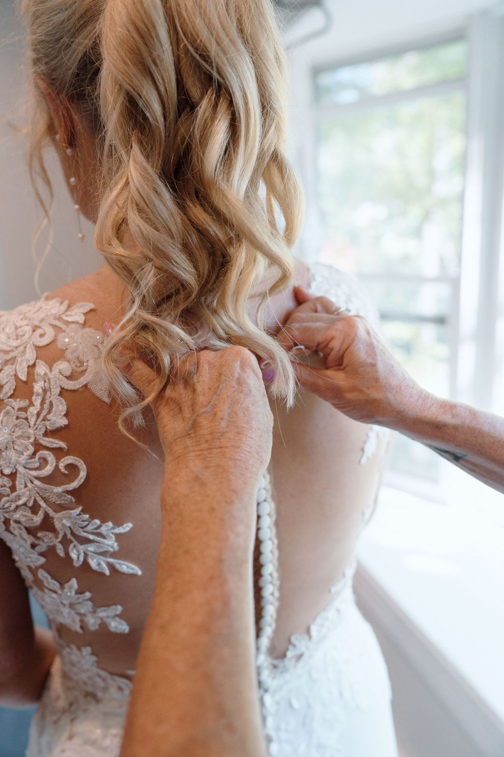 Close-up of intricate lace detail on back of wedding dress being fastened.