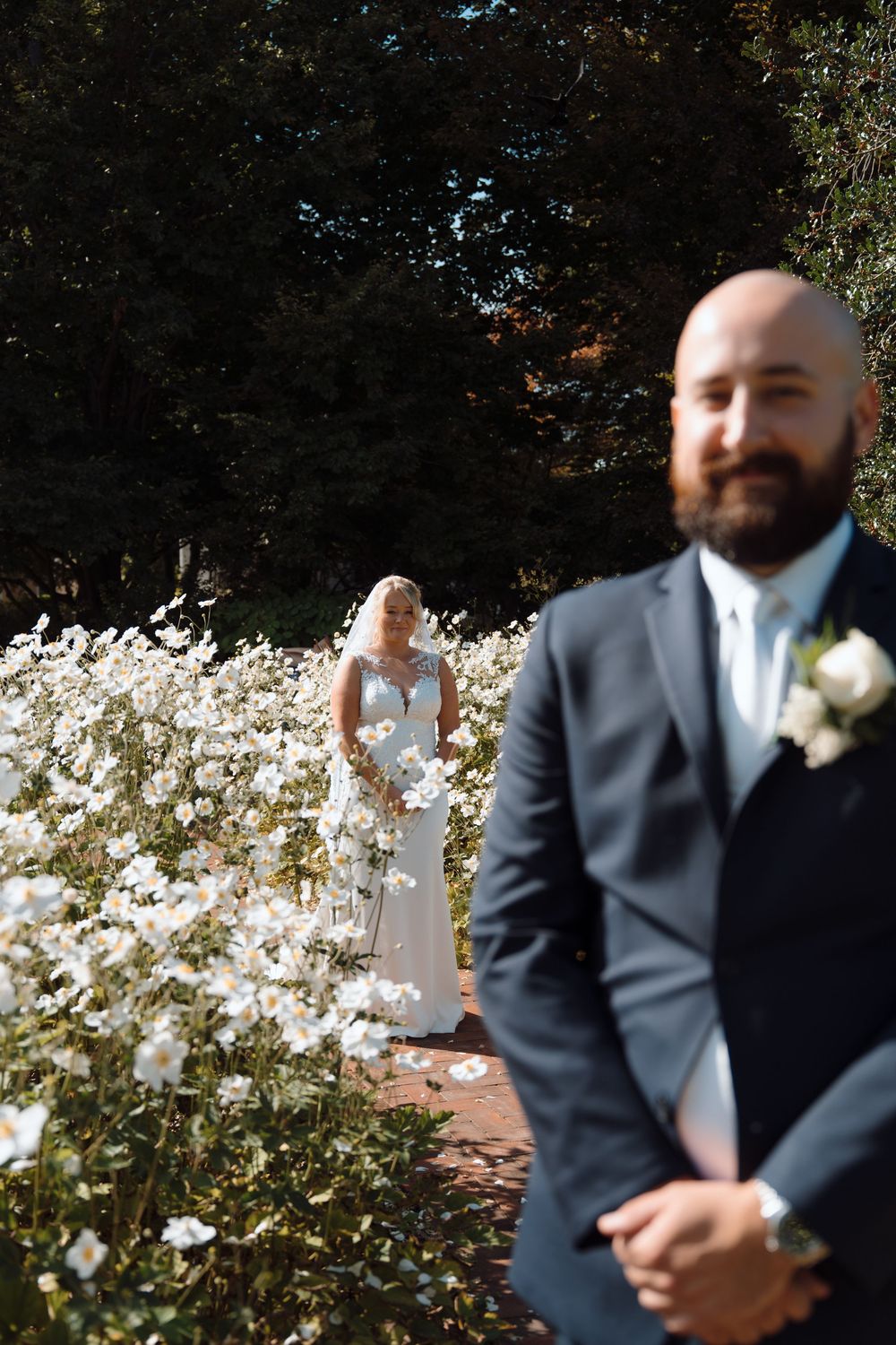 Wedding party members in formal attire posing among white flowers in a garden setting.