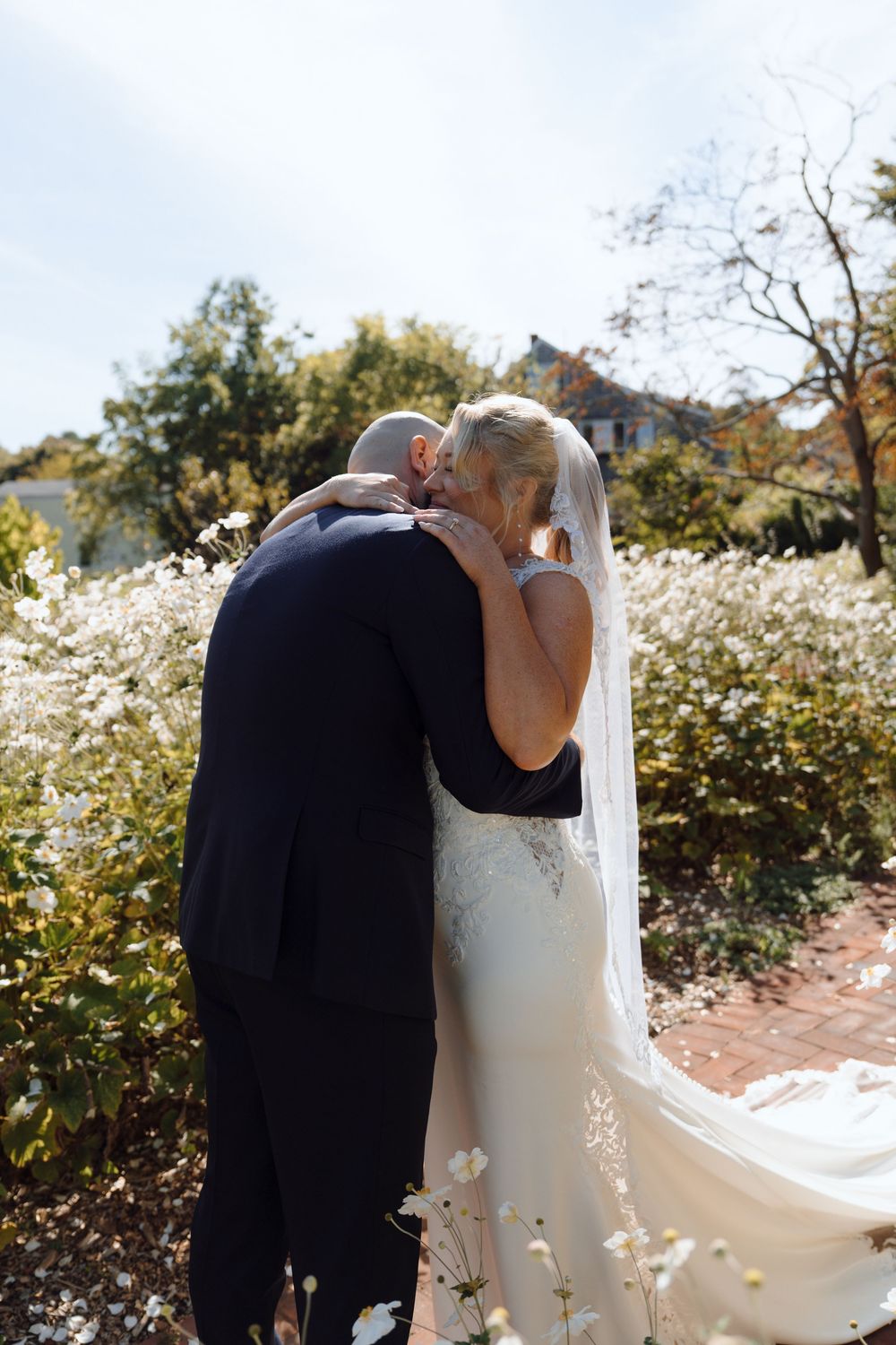 Romantic outdoor wedding moment in garden surrounded by white wildflowers on sunny day.