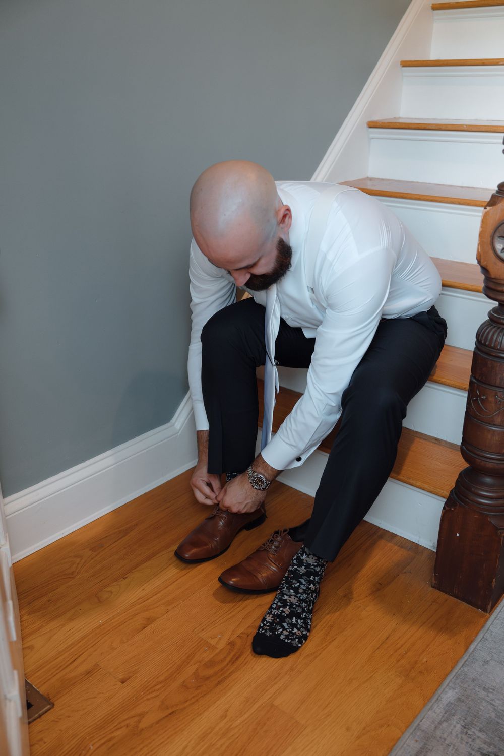 Person putting on dress shoes while sitting on wooden stairs.