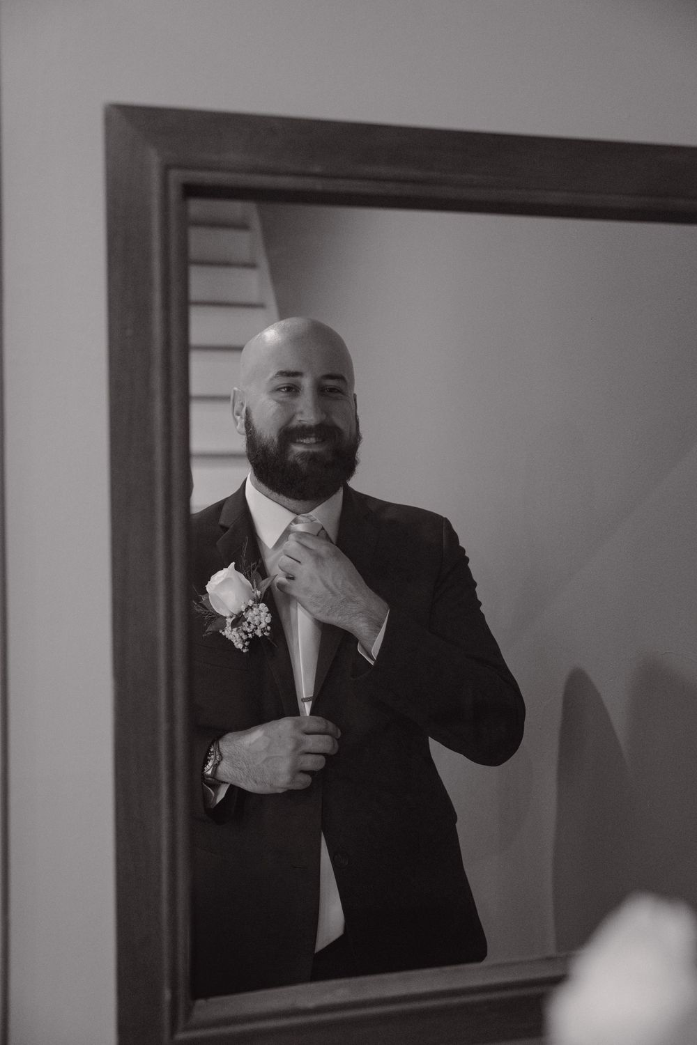 A formal black suit and tie ensemble with boutonniere being adjusted.