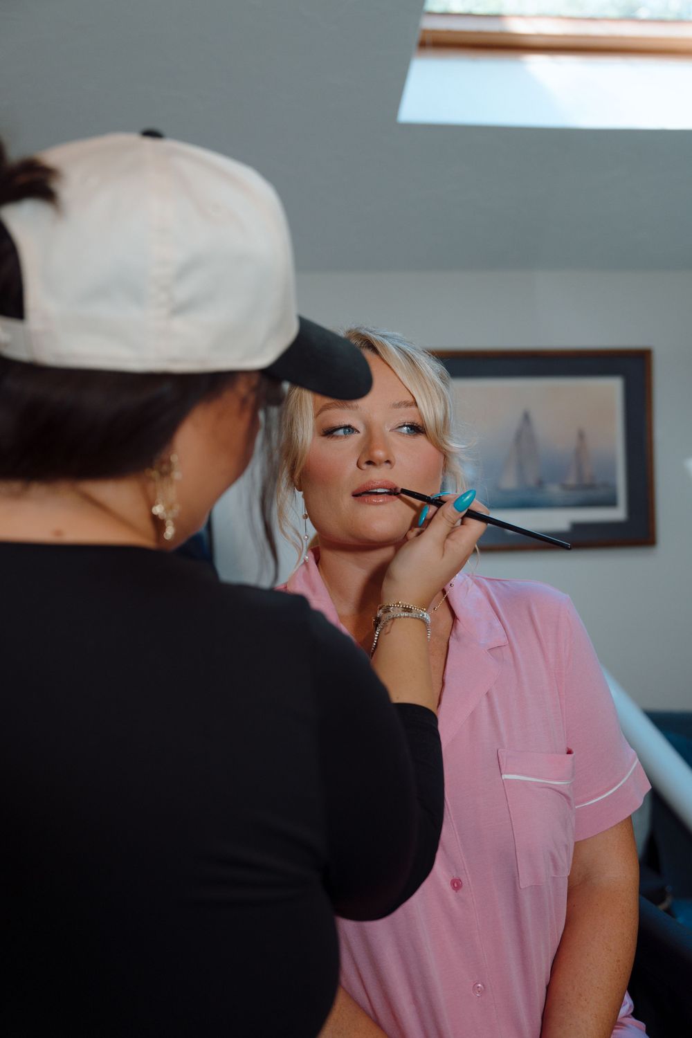A makeup artist applies cosmetics to a client wearing a pink shirt.