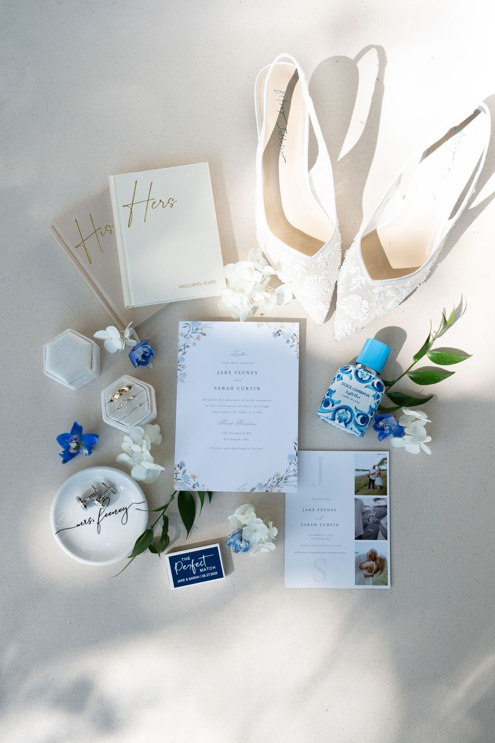 Wedding invitation suite with white and blue floral details displayed alongside elegant white heels and delicate flowers.