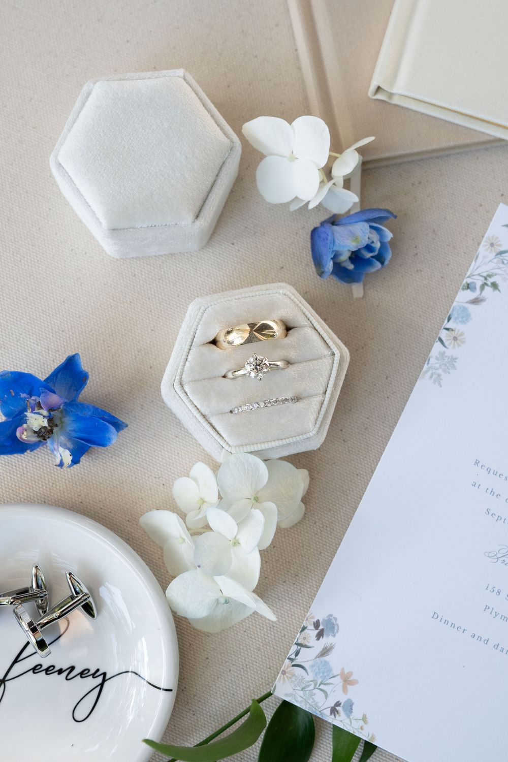 Wedding detail shot showing white and blue floral arrangements with hexagonal place cards on a beige surface.