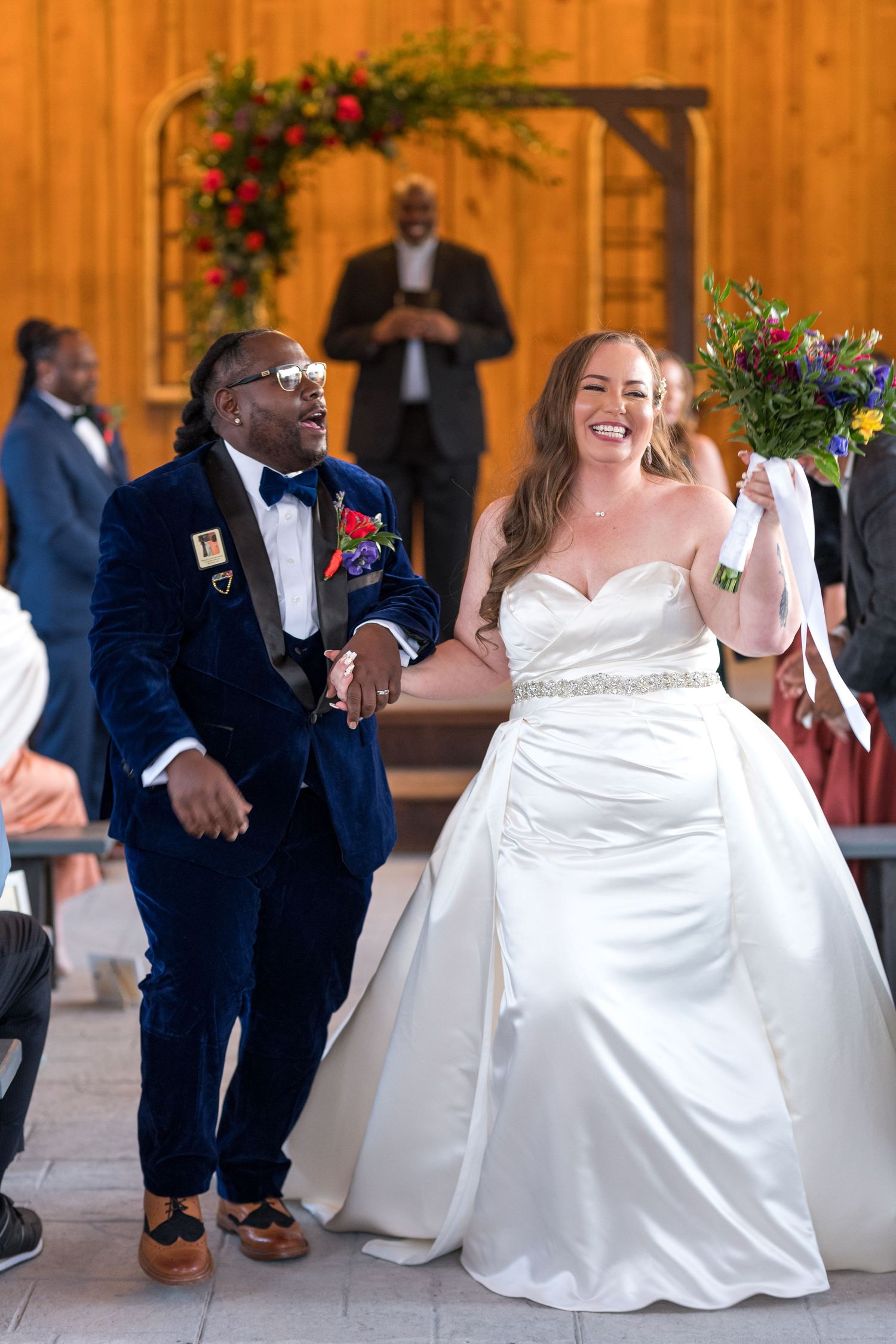 Wedding guests enjoy dancing and celebrating at a rustic barn venue decorated with red floral accents.
