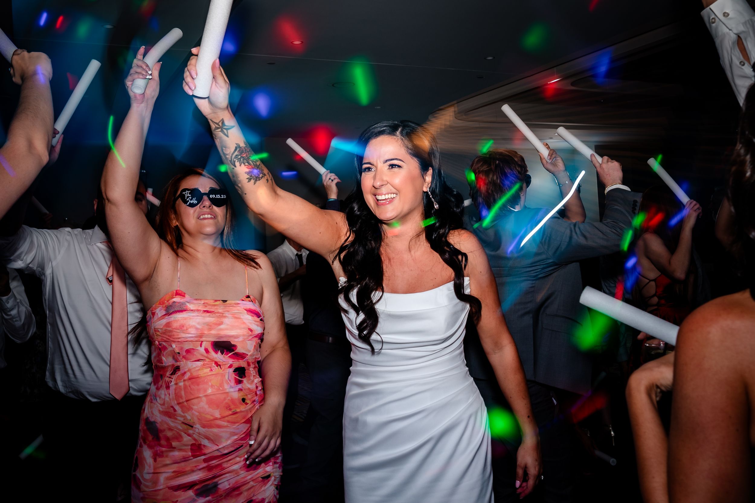 Wedding reception dance party with colorful lights and glow sticks on the dance floor.