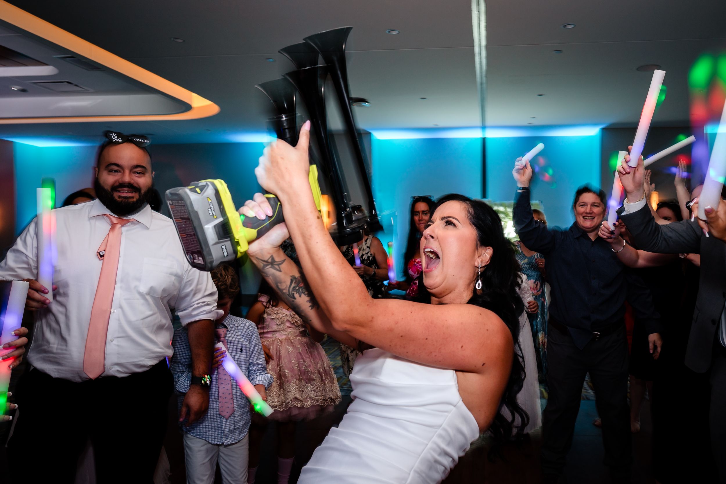 Energetic dancing and celebration at a wedding reception with blue ambient lighting.
