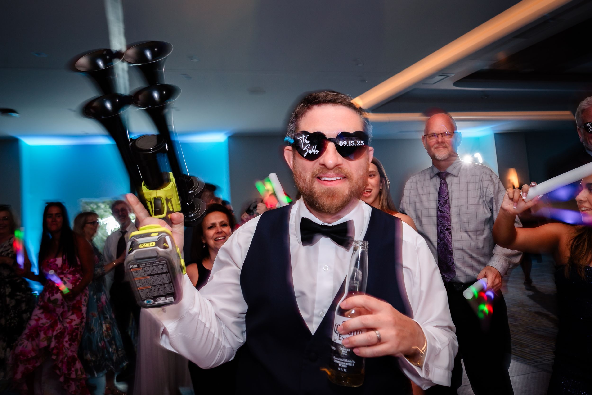 Wedding guests dancing and celebrating with sunglasses and formal attire.