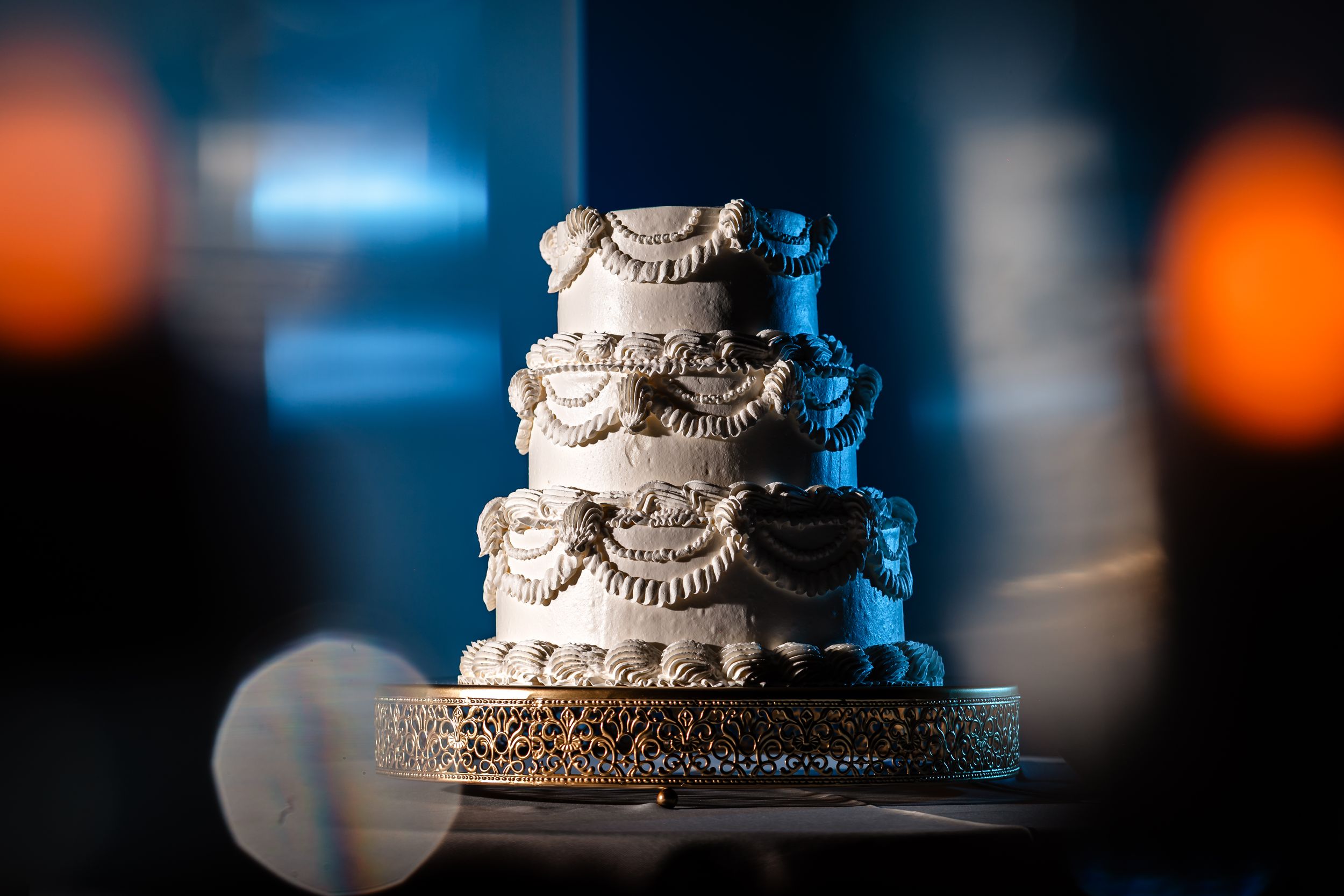 Elegant white wedding cake with ornate details displayed with dramatic lighting.