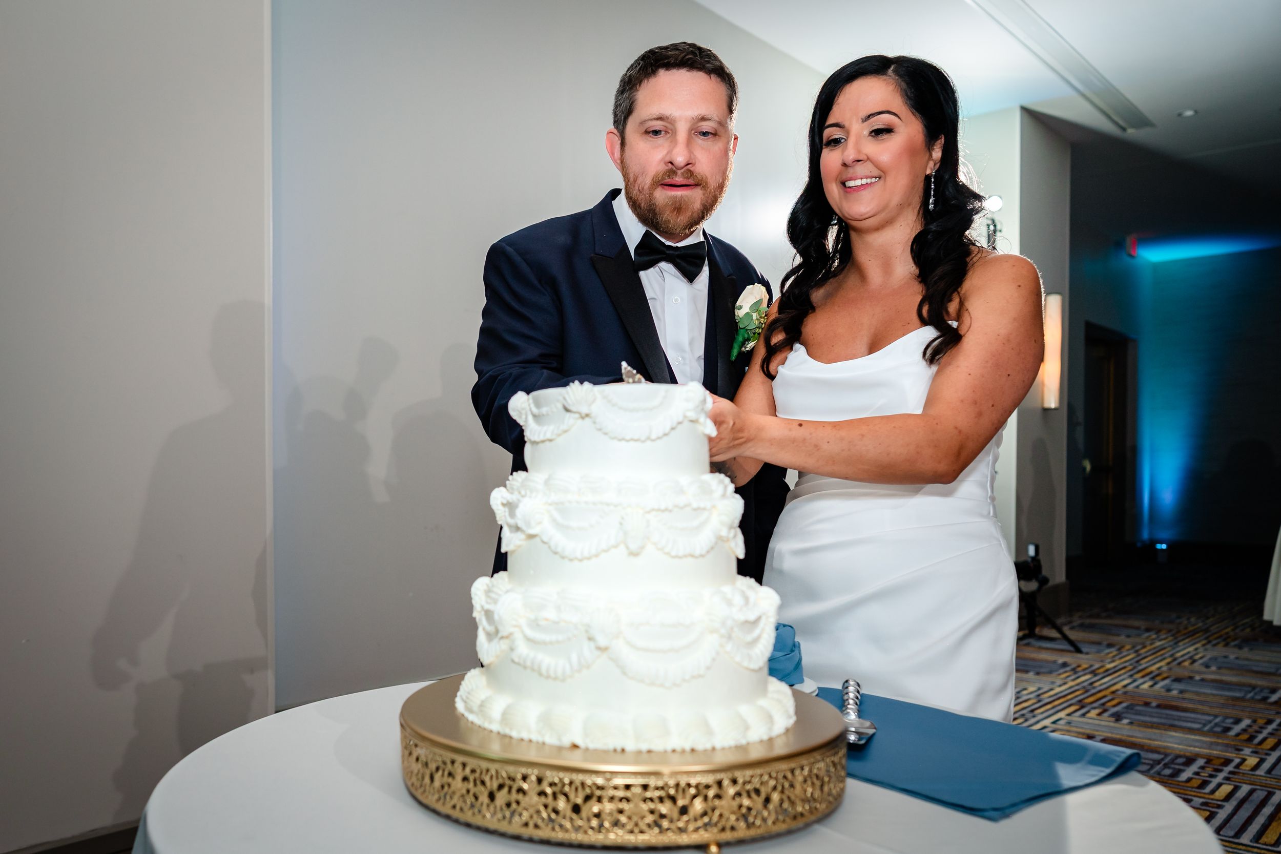 Traditional white wedding cake cutting ceremony with decorative gold stand.