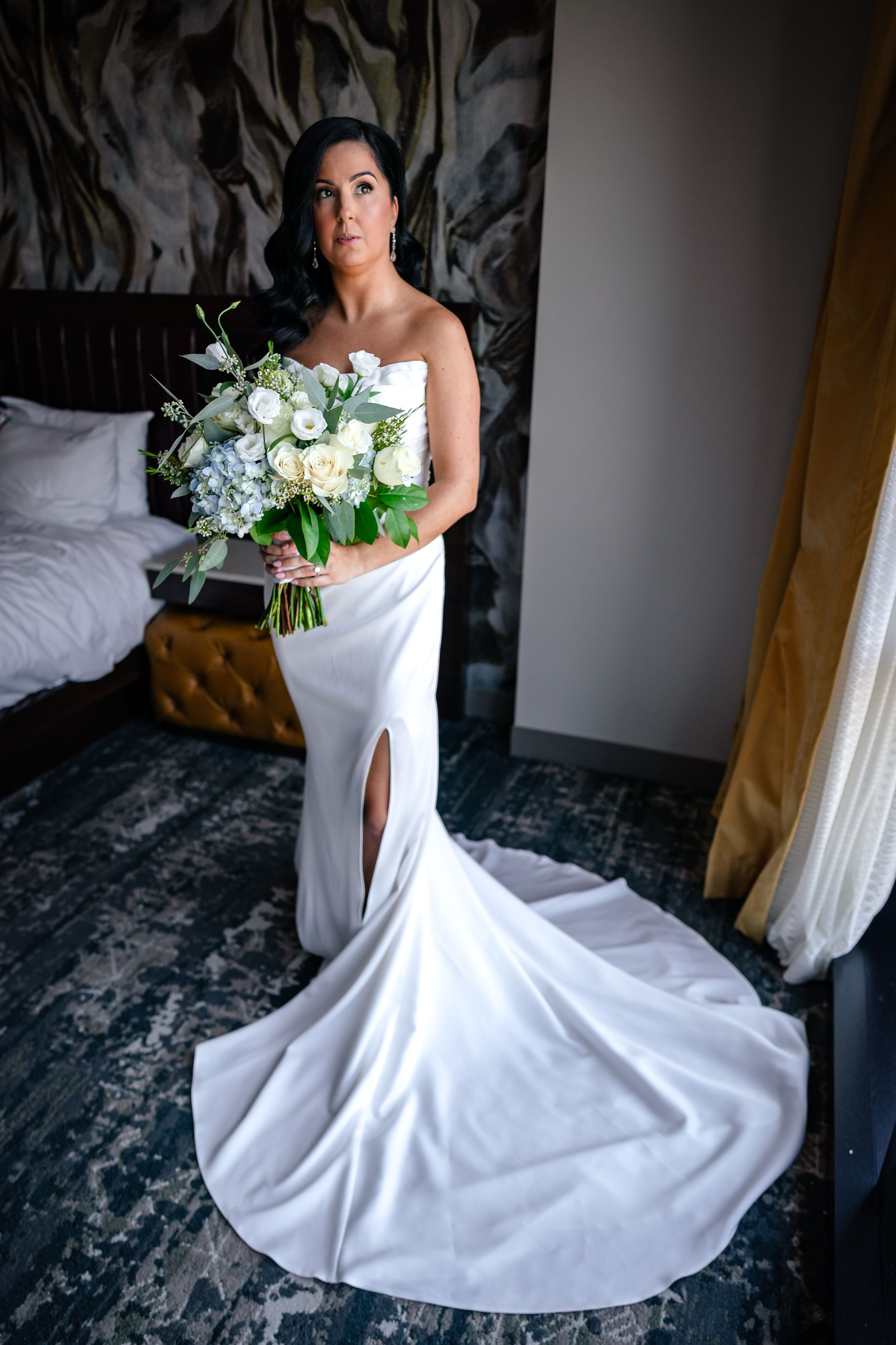 Bride in stunning white mermaid wedding gown holding elegant floral bouquet.