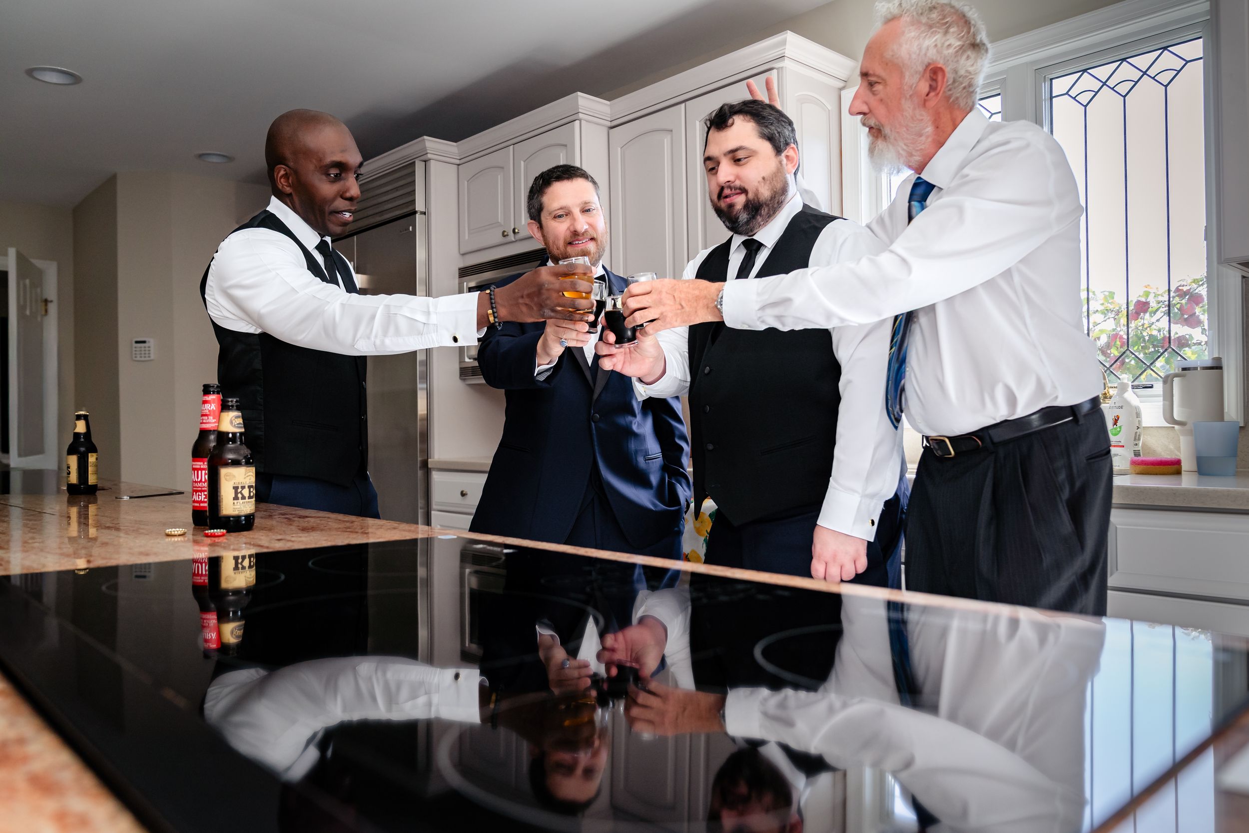 Wedding party members gather around a counter sharing drinks and conversation.