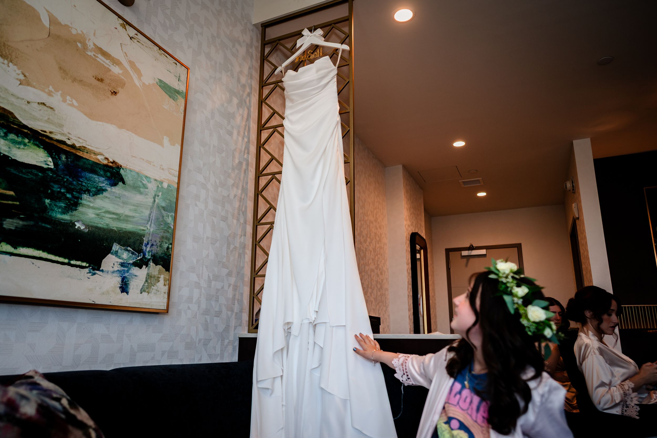 Wedding dresses and formal attire hanging in preparation room with warm lighting.