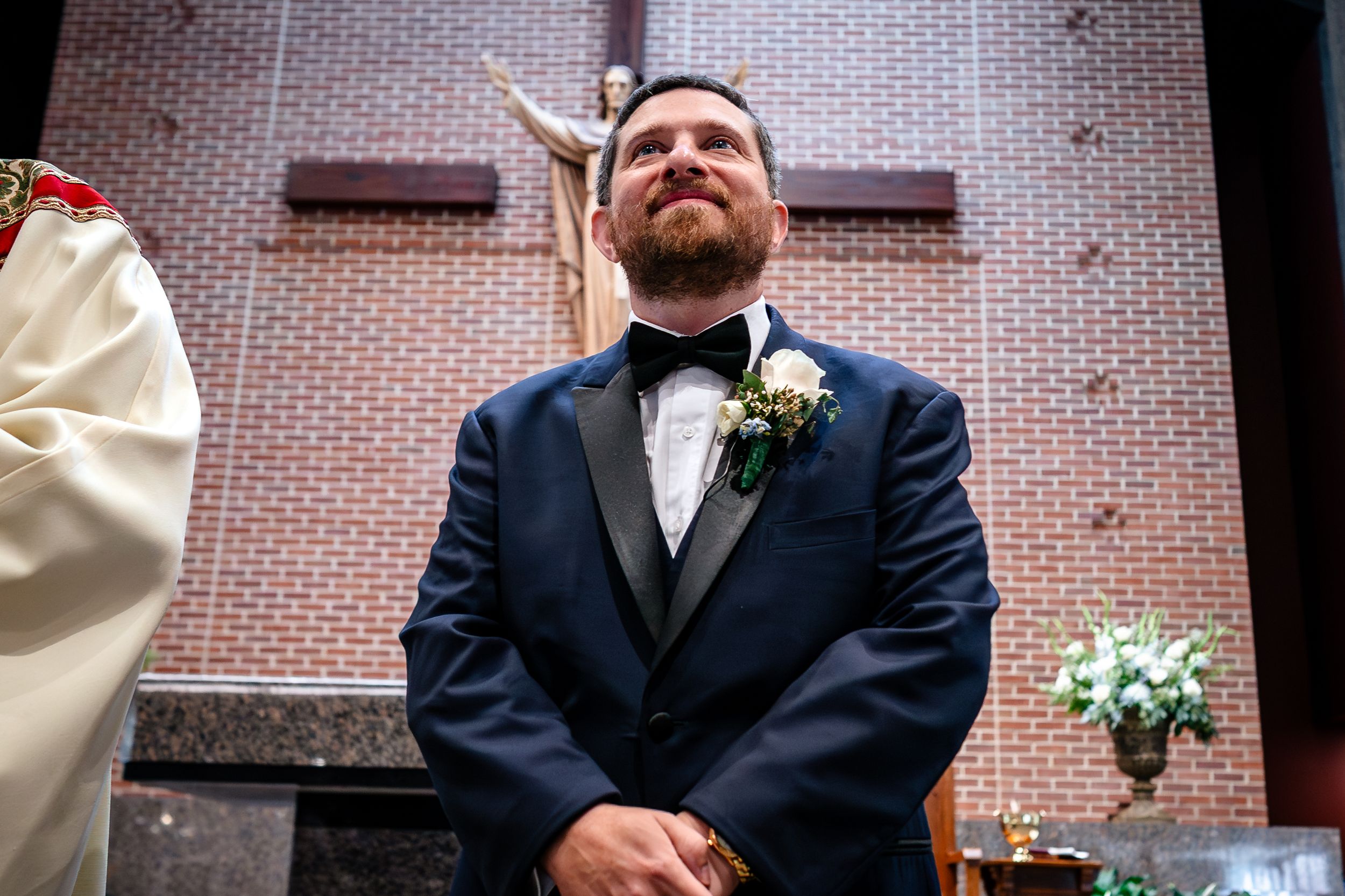 Wedding ceremony participants standing at the altar in a brick-walled church.