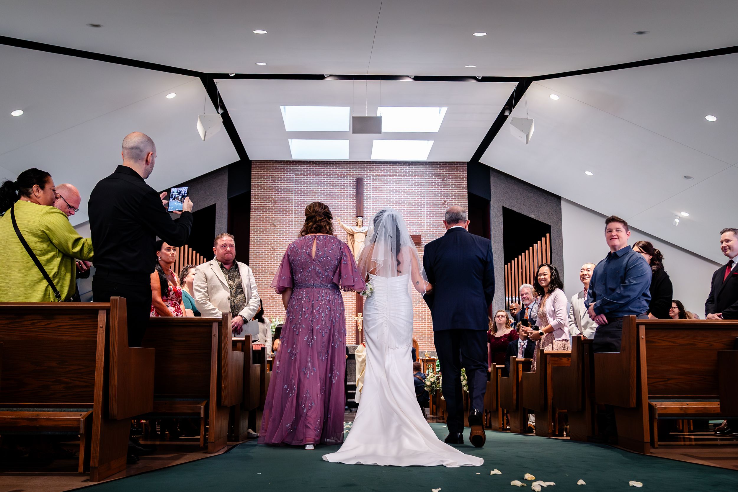 Wedding ceremony in progress inside a church with wooden pews and bright lighting.