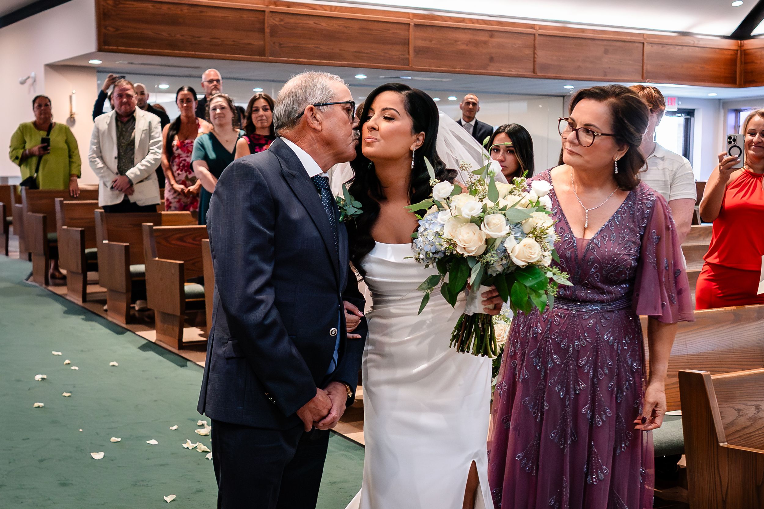Wedding party and guests celebrating in a church aisle with scattered flower petals.