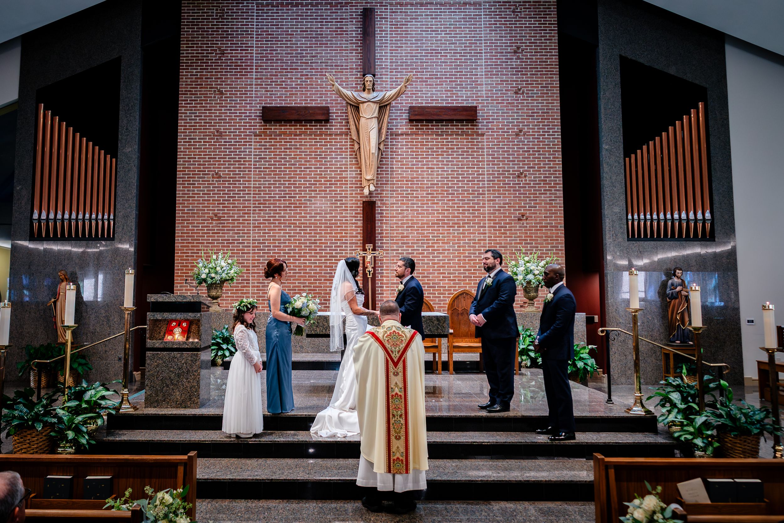 Wide view of church sanctuary during wedding ceremony with crucifix and organ pipes.