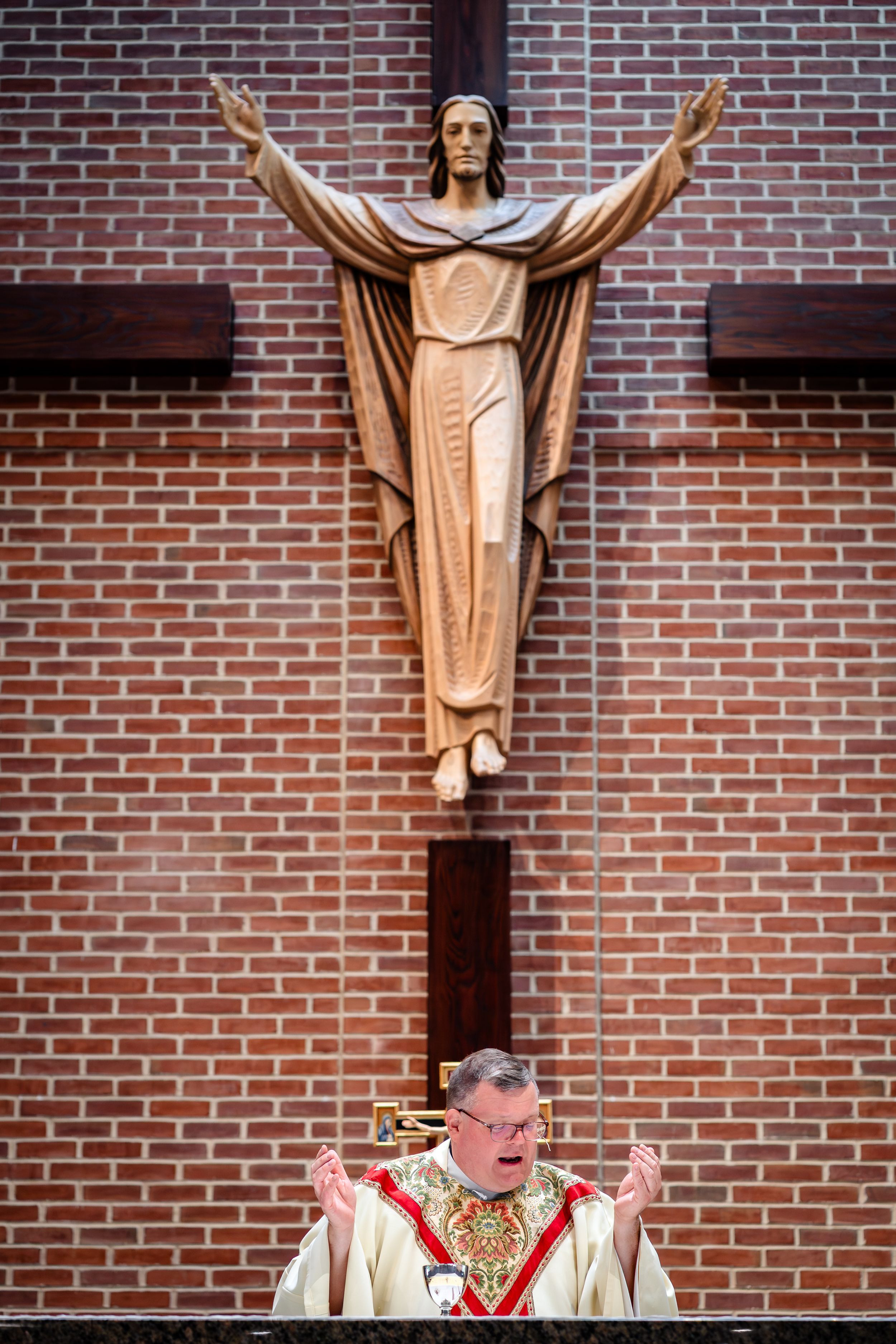 Large wooden crucifix mounted on red brick church wall during religious ceremony.