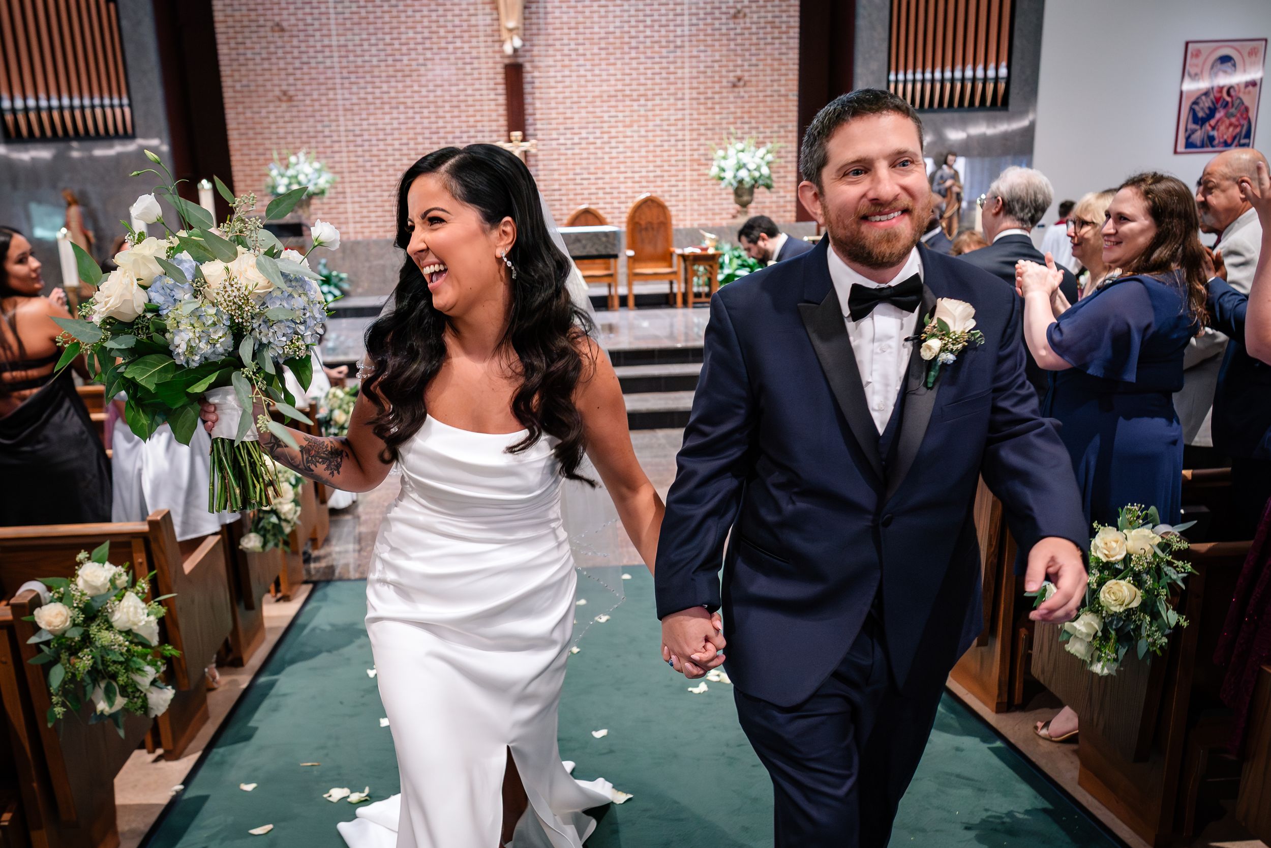 Wedding party celebrating with joy as they walk down church aisle with white floral decorations.