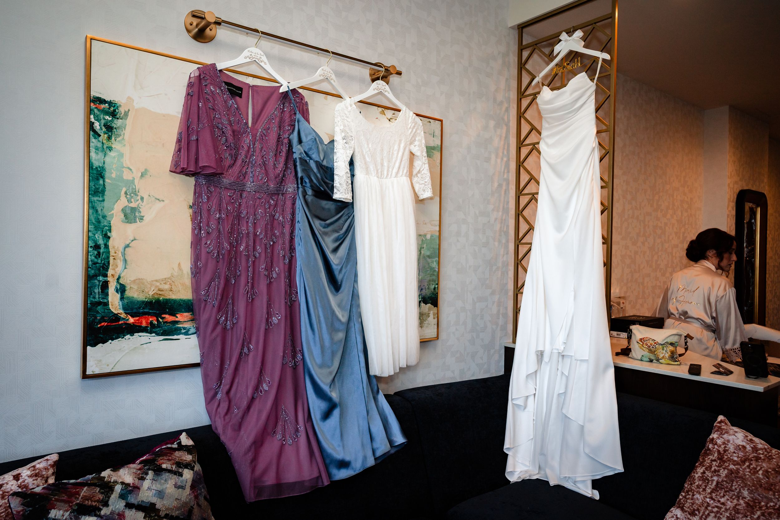 Purple and white formal dresses displayed on hangers against a beige wall.