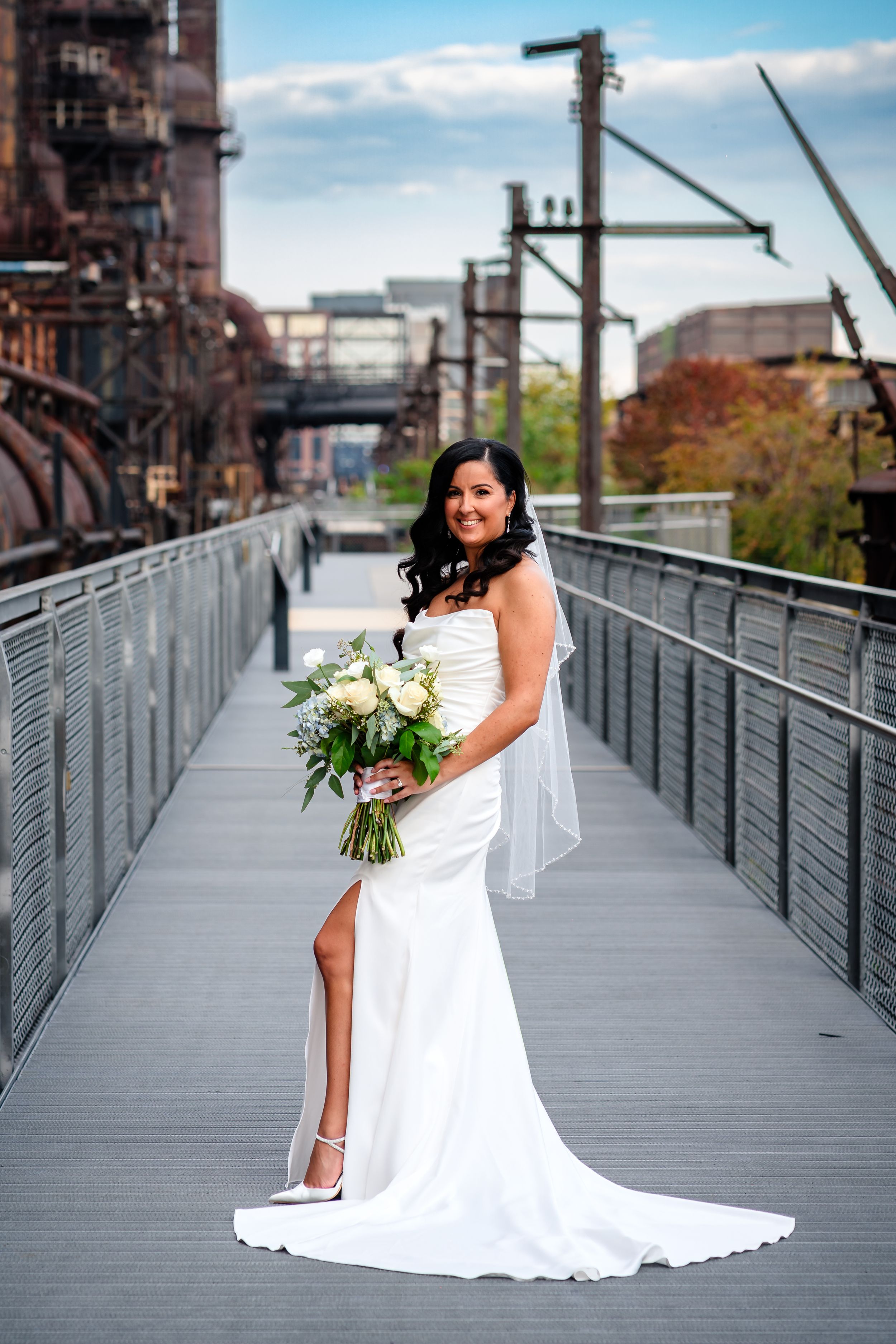 A person in a white wedding dress holds a bouquet on a metal walkway.