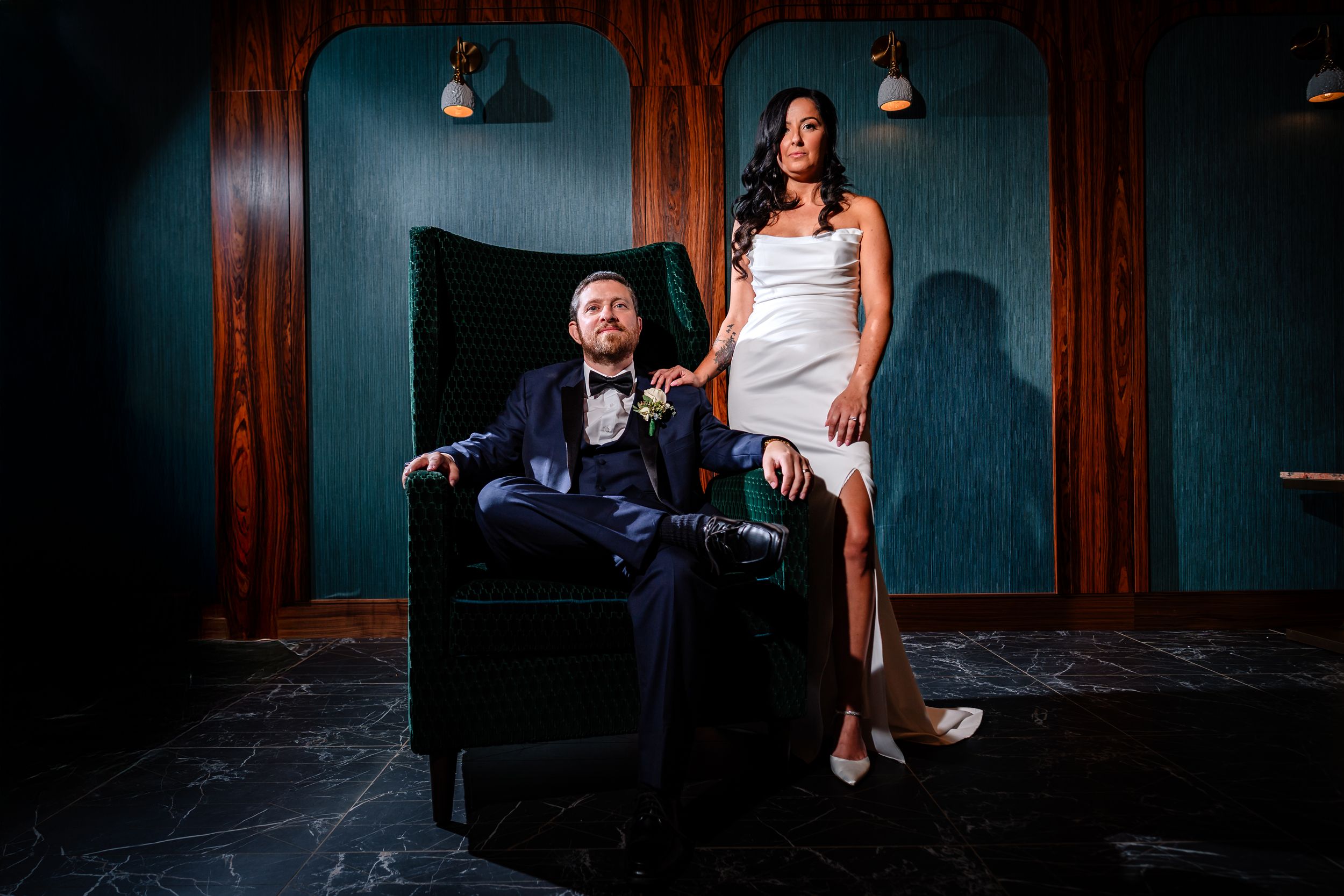 A couple poses in dramatic lighting against a dark wood-paneled wall.