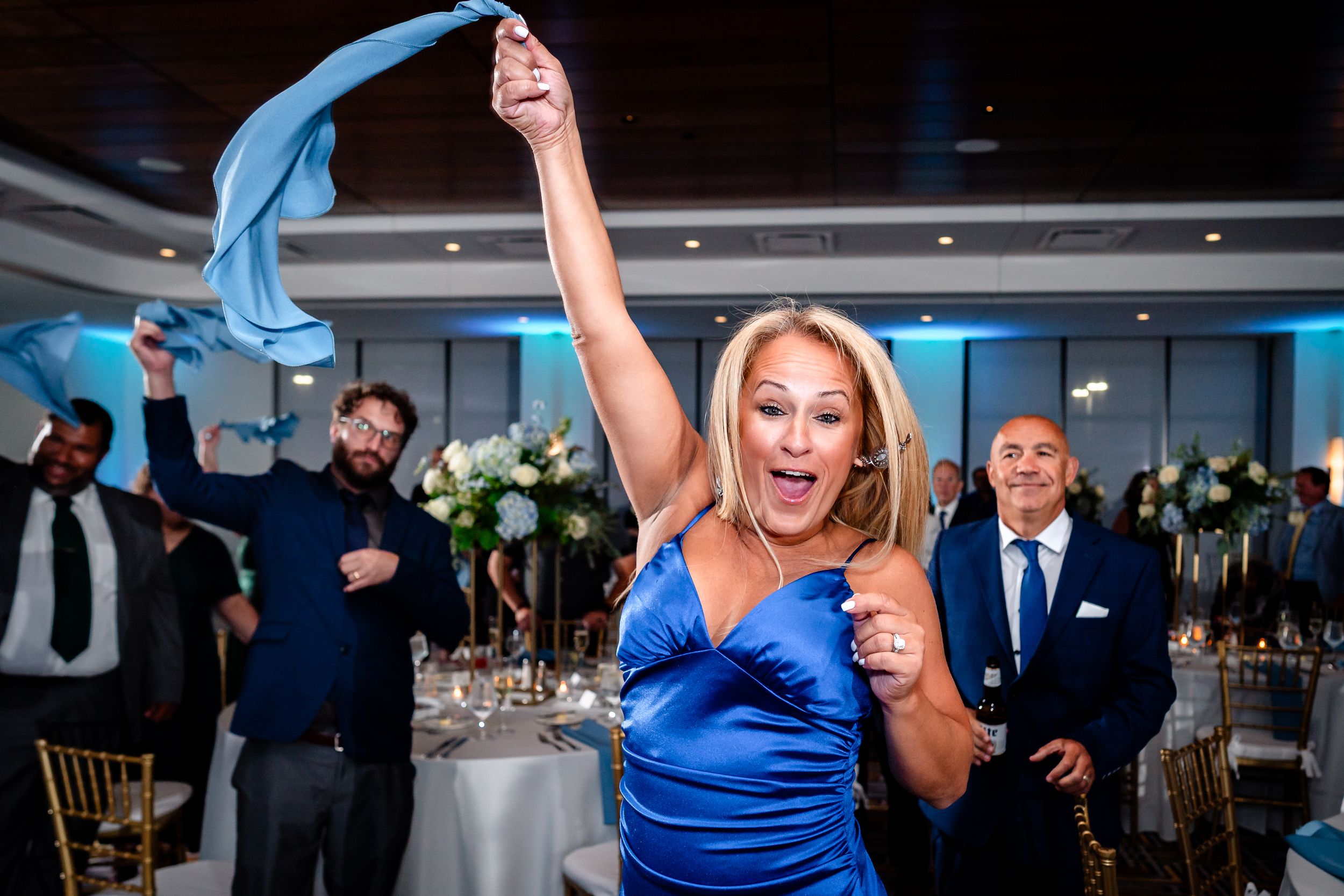 Energetic dancers in formal attire perform during a wedding reception with blue uplighting.