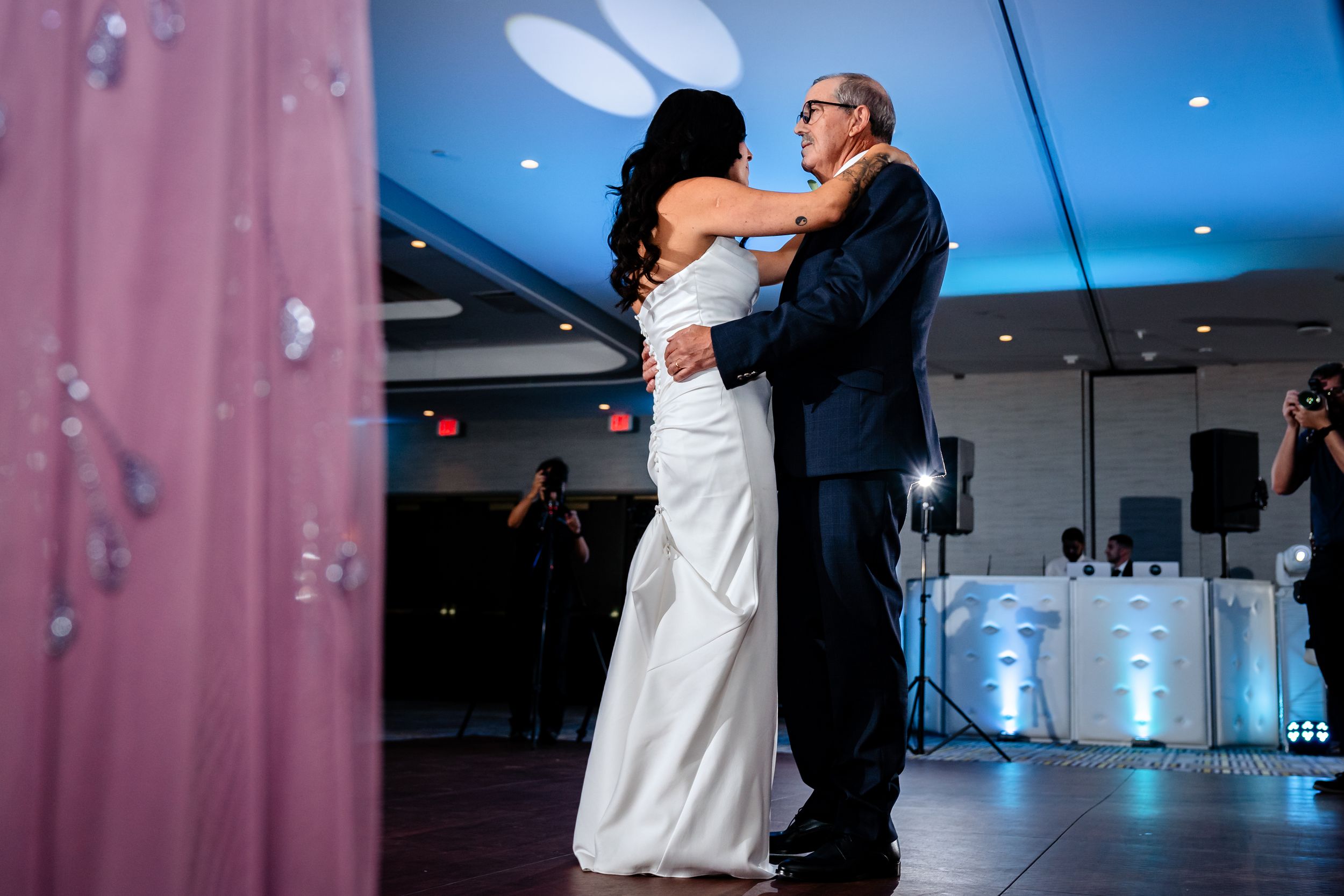 Wedding reception dance floor filled with couples under dramatic blue and pink lighting.