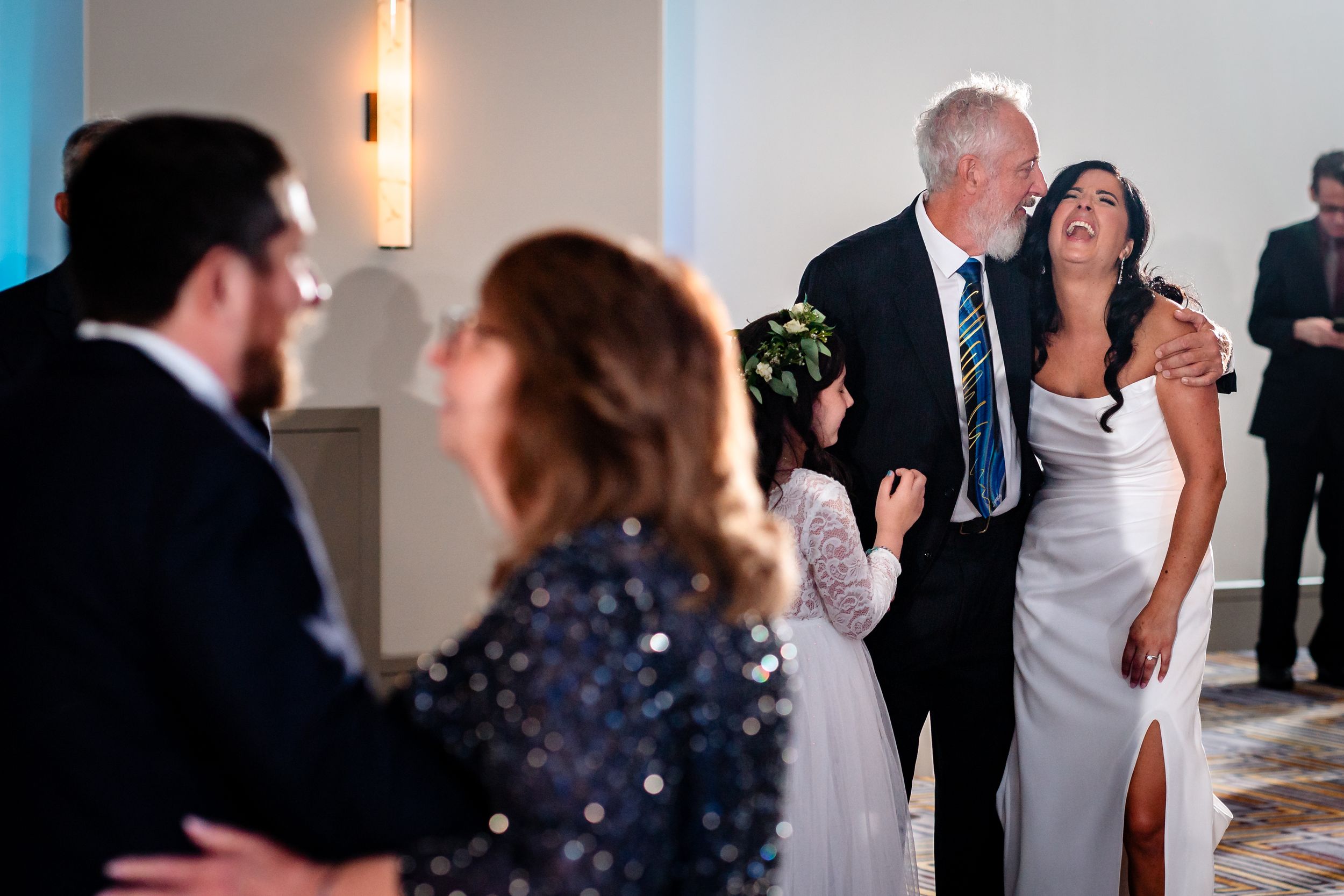 Wedding reception guests dance in formal attire under elegant venue lighting.