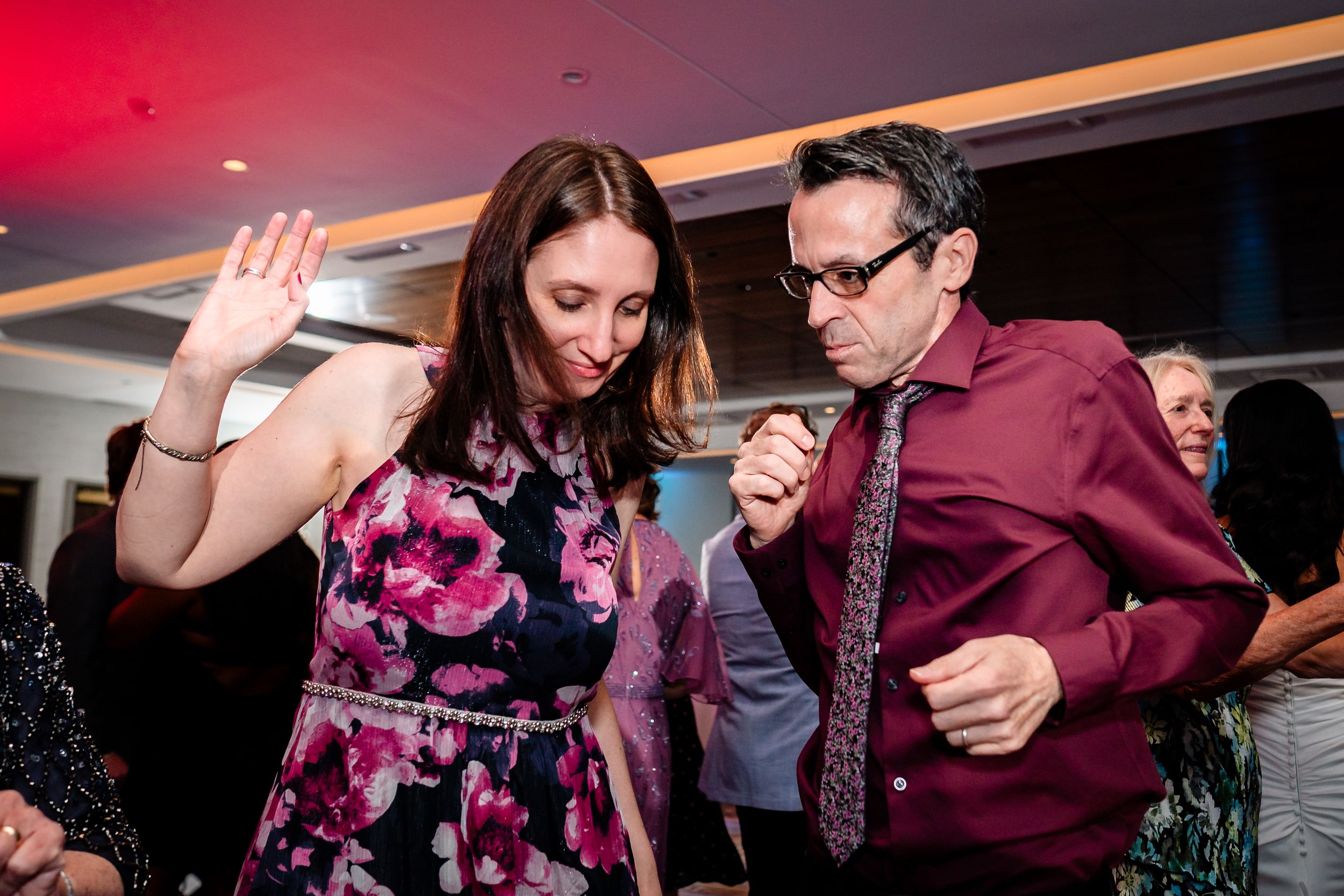 Wedding guests dancing and celebrating at a reception with dramatic red lighting.