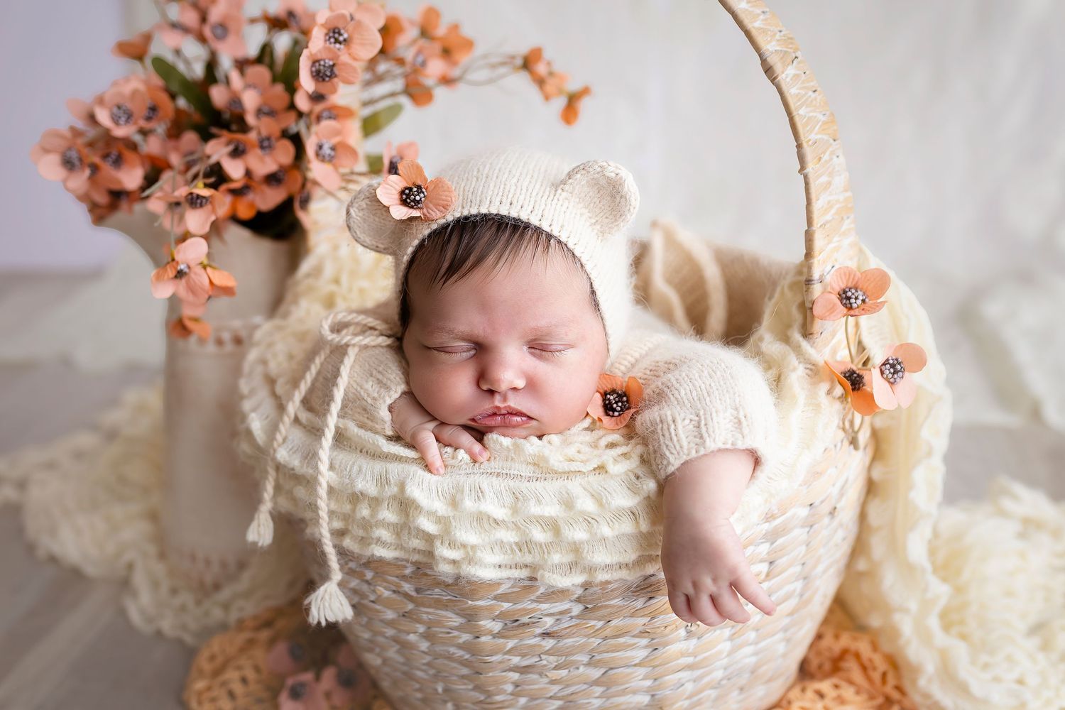 bebe vestida de oso dentro de una canasta redonda rodeada de flores colores son crema y terracota fotografia acercada