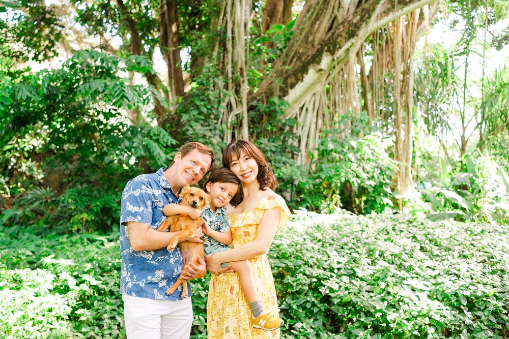 A couple and their golden retriever dog pose together in a lush green outdoor setting during a photo session.