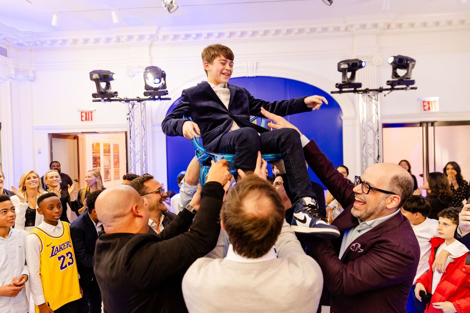 A crowded room of people dancing and celebrating at a festive indoor event with bright lighting.
