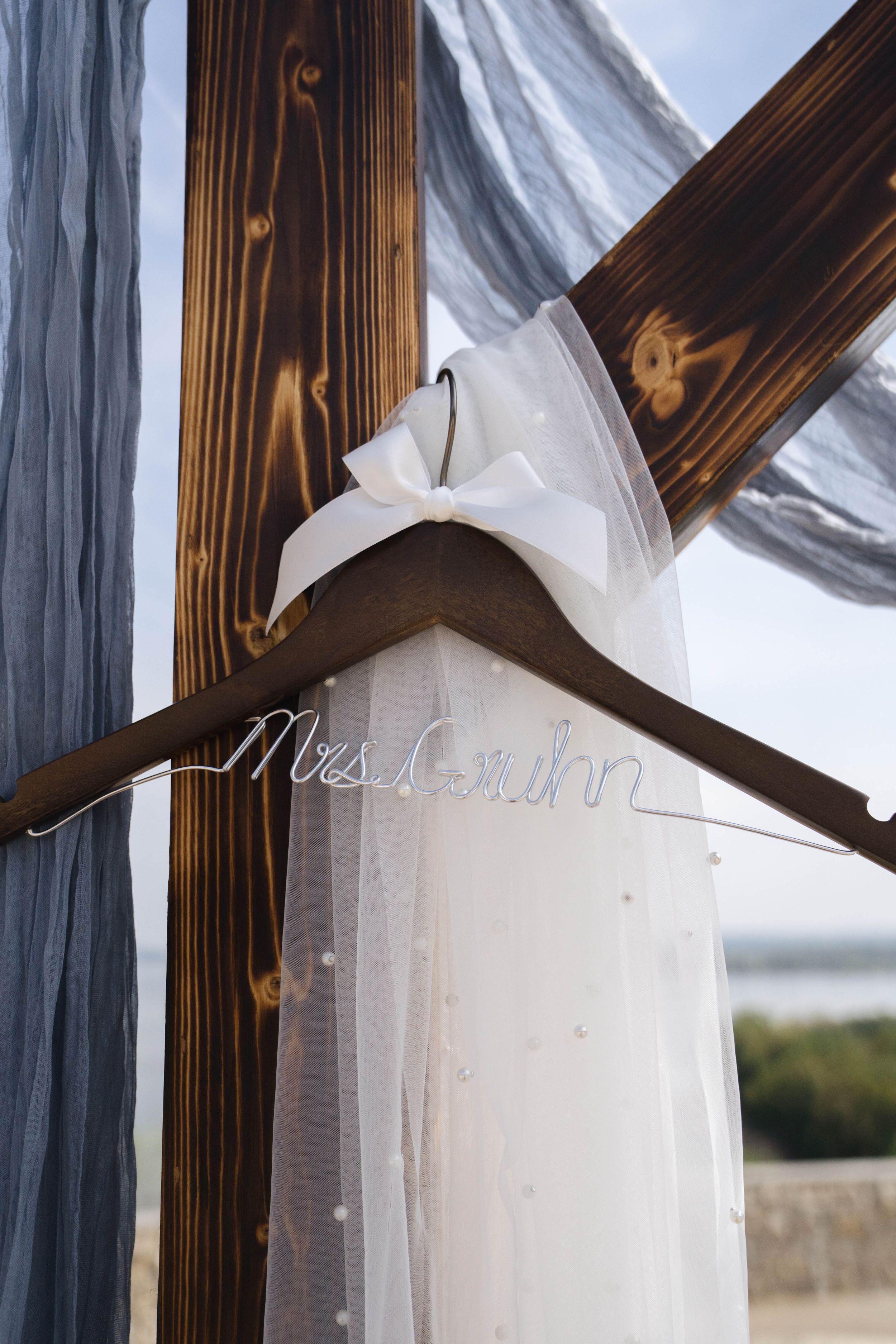 White wedding dress veil hanging against rustic wooden backdrop with decorative text.