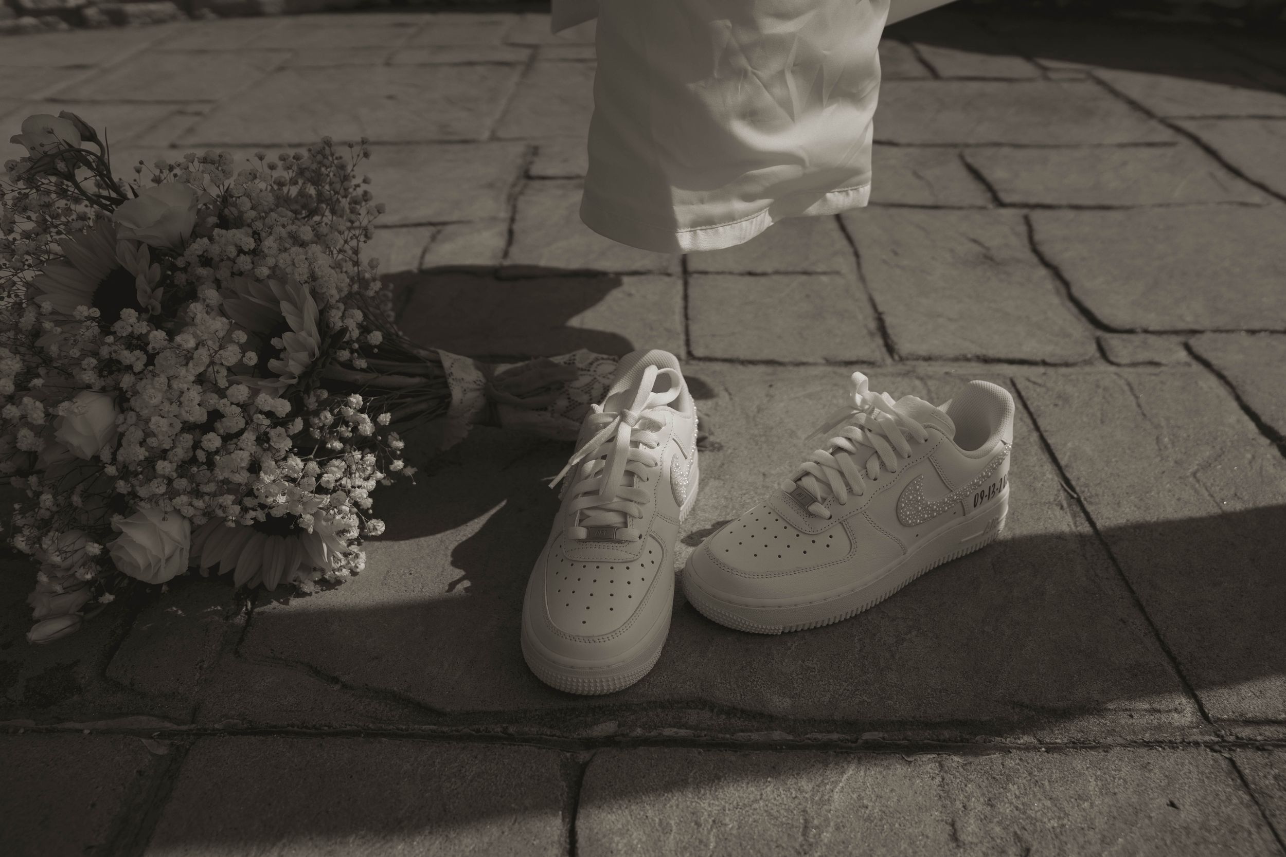 Close-up of white sneakers and dress hem on stone patio during wedding ceremony.