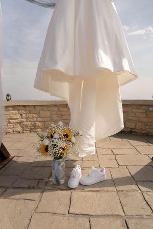 White wedding dress and sunflower bouquet on stone patio under bright sky.
