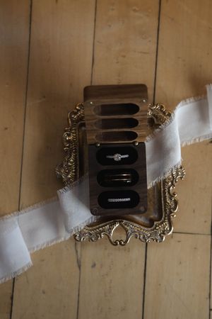 Ornate vintage-style camera strap clips with decorative metallic details against a wooden background.