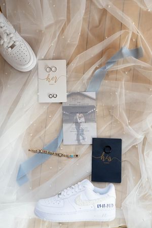 Wedding details flatlay with white sneakers, invitations and sheer fabric in soft neutral tones.