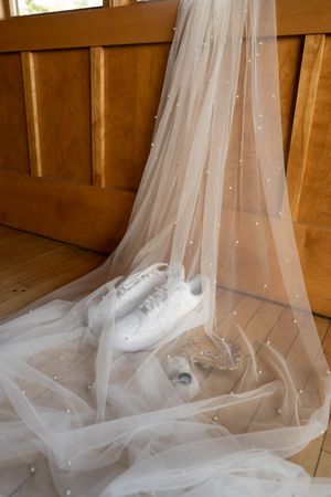 Delicate white tulle wedding veil with sparkly details draped elegantly against a wooden background.