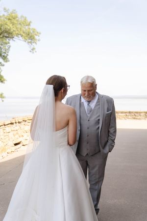 Emotional first look moment between bride in white dress and father in grey suit.