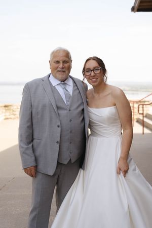 Bride in classic white gown poses with father in grey suit during outdoor wedding portraits.