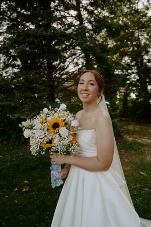 Bride holding vibrant sunflower and baby's breath bouquet in a classic white wedding gown.