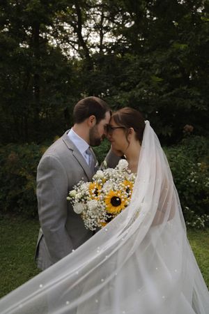 Romantic wedding portrait with flowing veil and sunflower bouquet in garden setting.