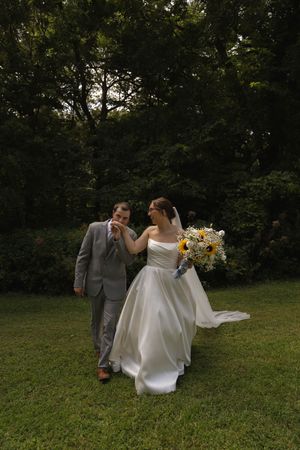 A playful wedding photo of newlyweds laughing together while holding a sunflower bouquet.